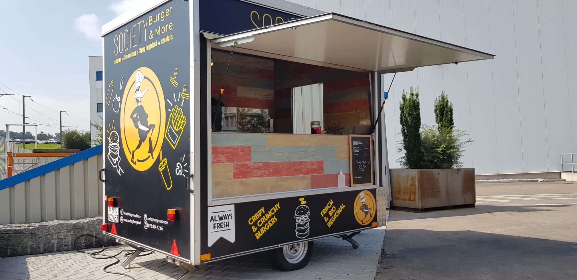 Ein schwarzer Society Foodtrailer mit geöffneter Ausgabeklappe